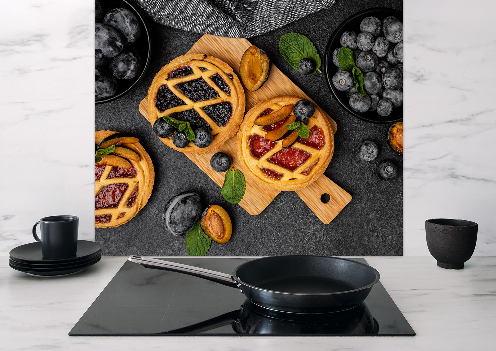 Spritzschutz "Kuchen" mit bunten Gebäckstücken und frischen Beeren auf einem Holzbrett, Küchenutensilien im Vordergrund.