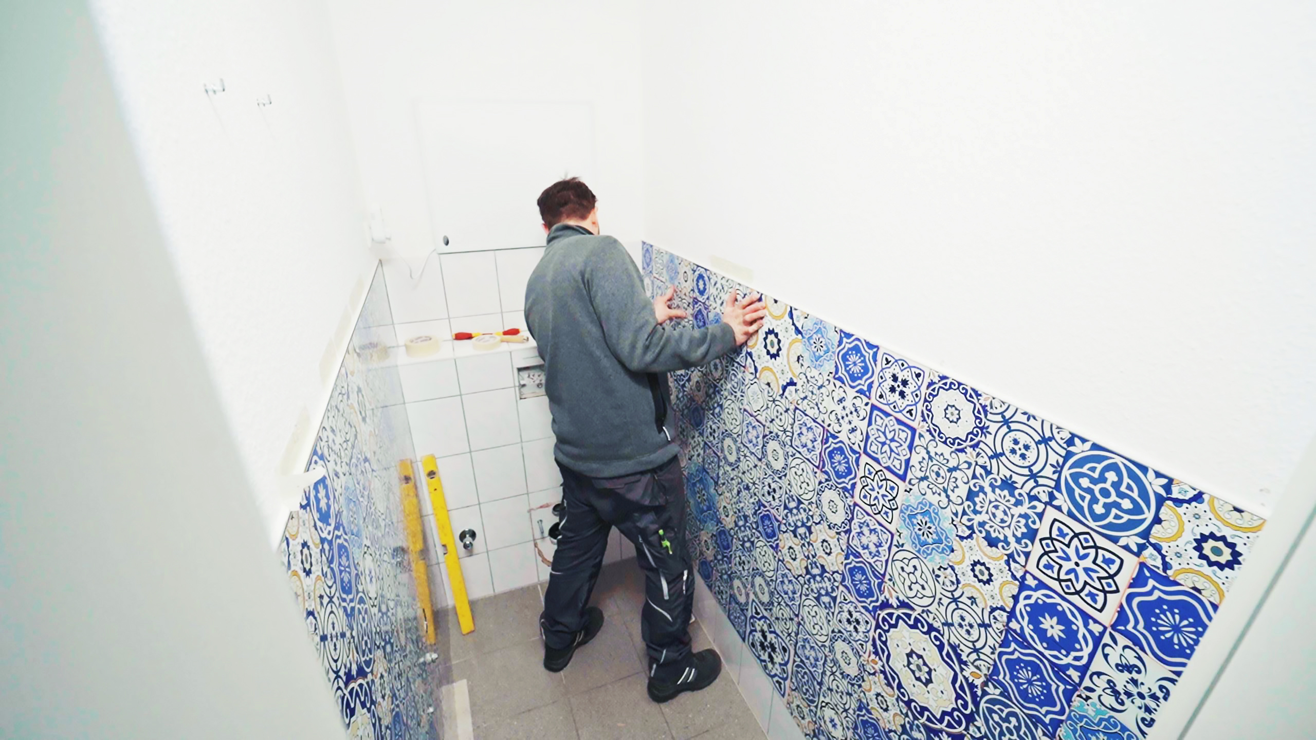 Ein Handwerker bringt bunte Fliesen an einer Wand an, während er sich leicht nach vorne beugt.