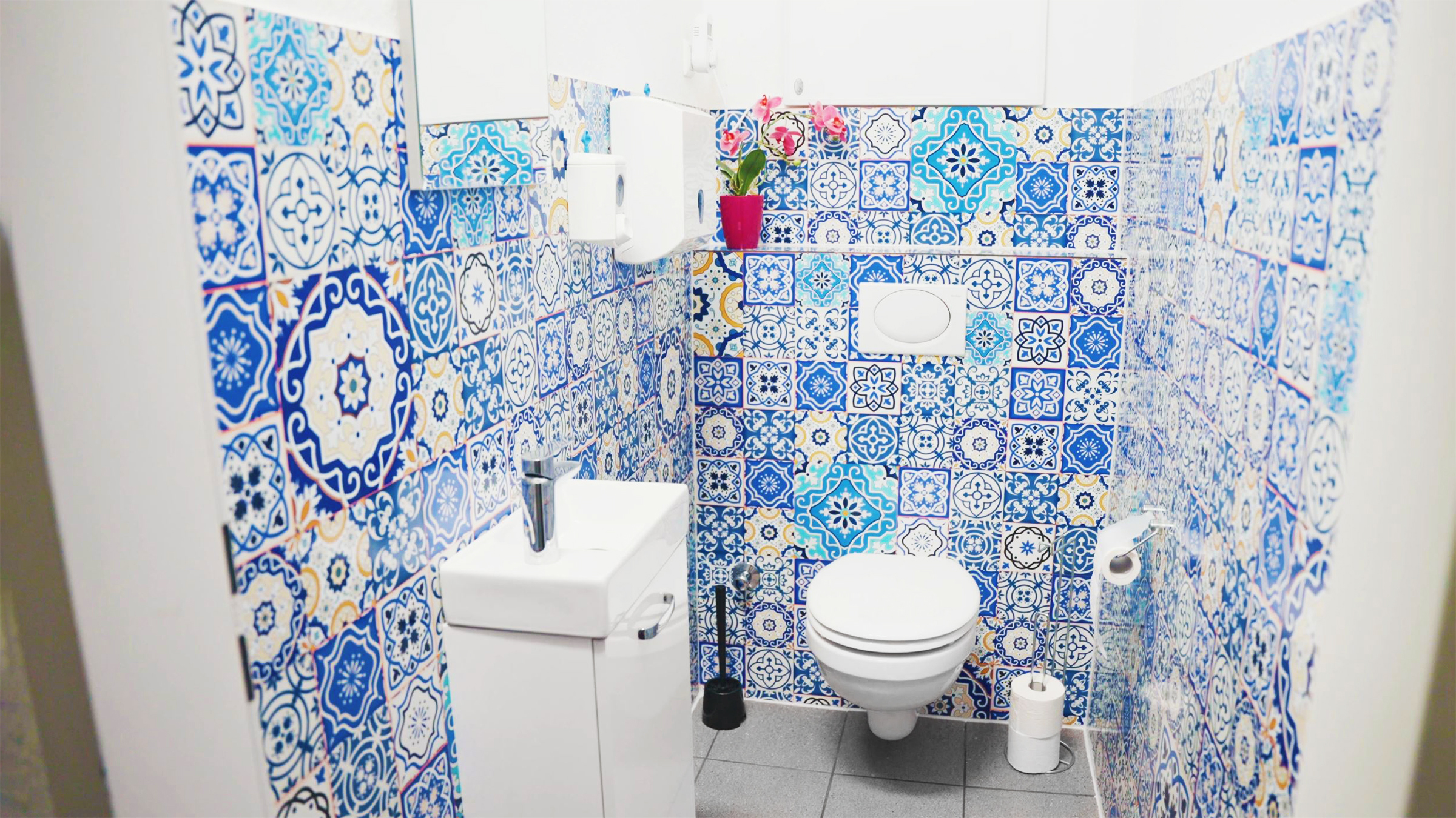 Badezimmer mit bunten Fliesen in Blau- und Weißtönen, WC und Waschbecken sichtbar.