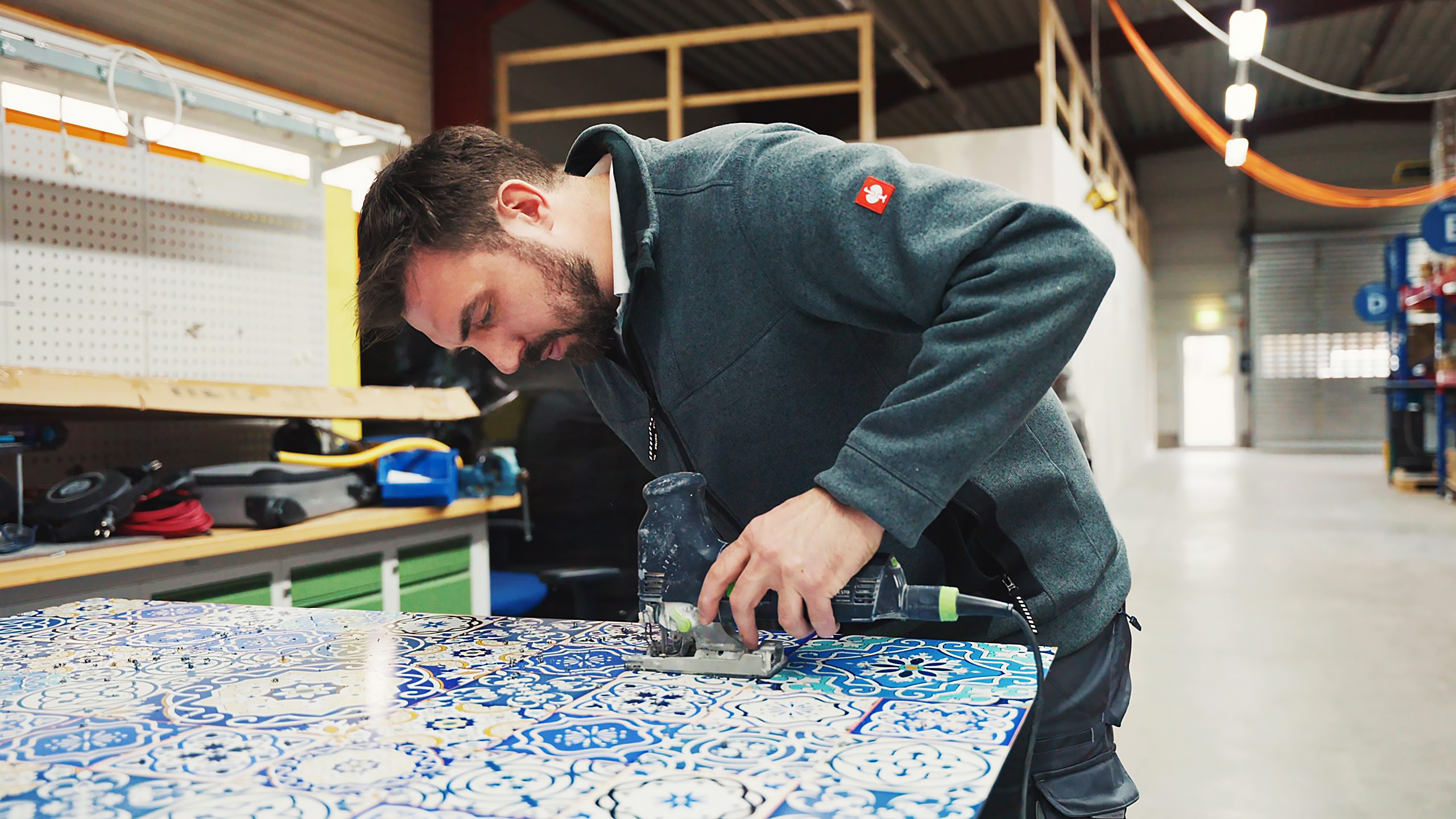 Ein Mann schneidet eine dekorative Platte mit einer elektrischen Säge in einer Werkstatt.