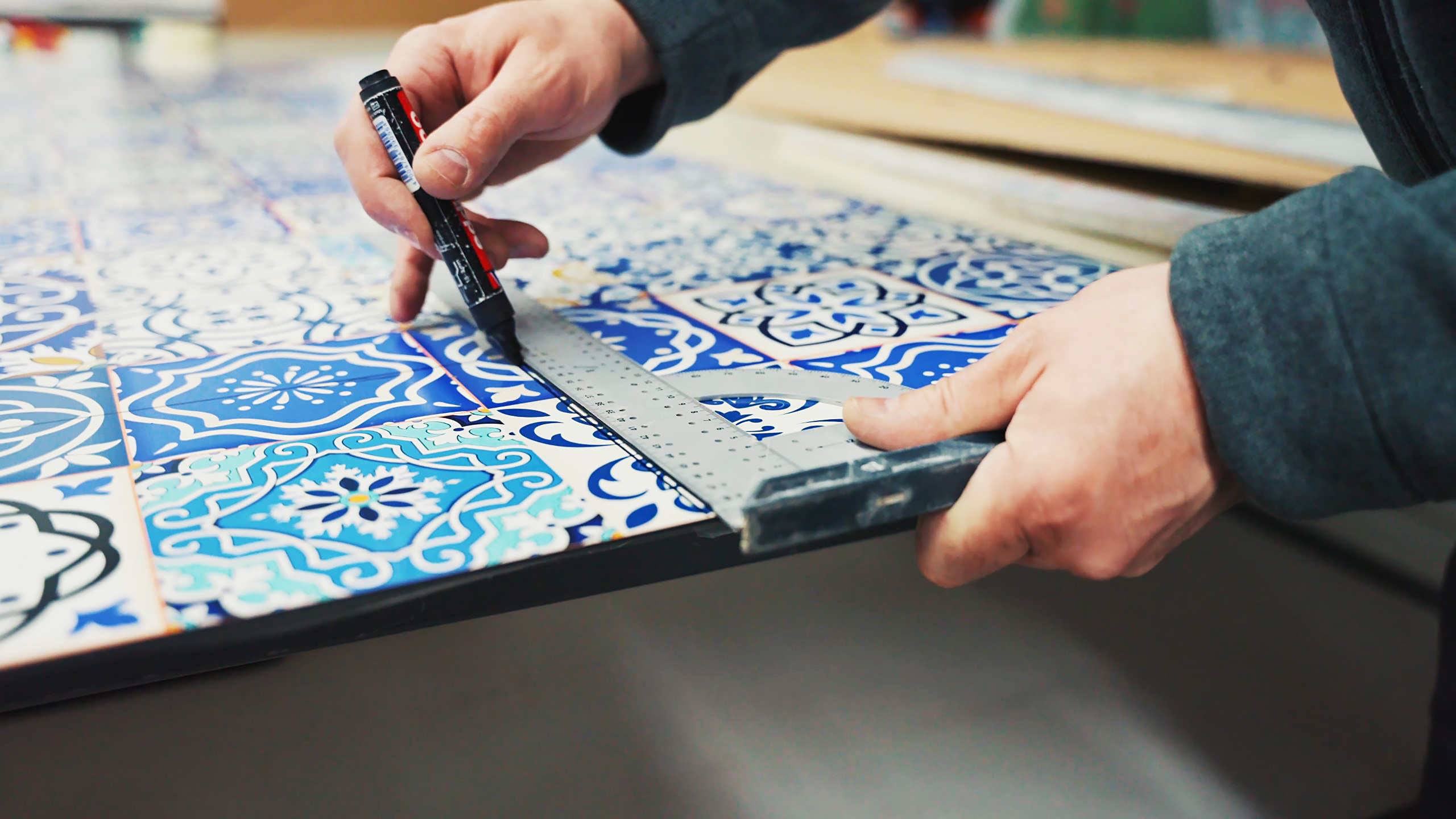Hände markieren Fliesen mit einem Marker und einem Metalllineal auf einem Tisch.