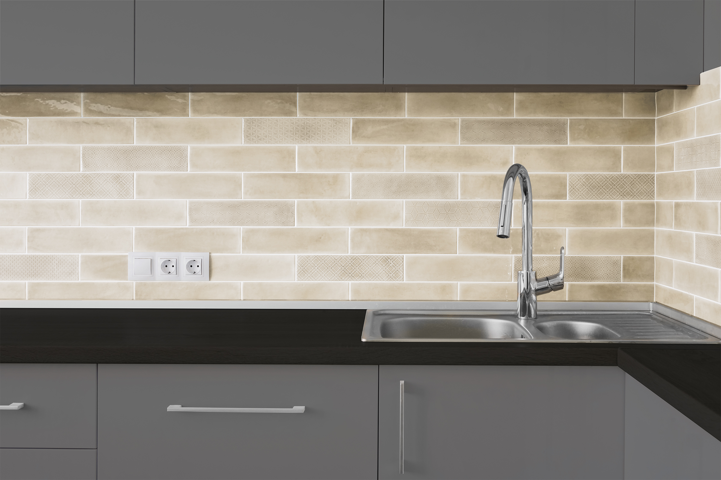 Vorher-Bild einer modernen Küche mit grauen Schränken, schwarzer Arbeitsplatte und beige Fliesenrückwand.