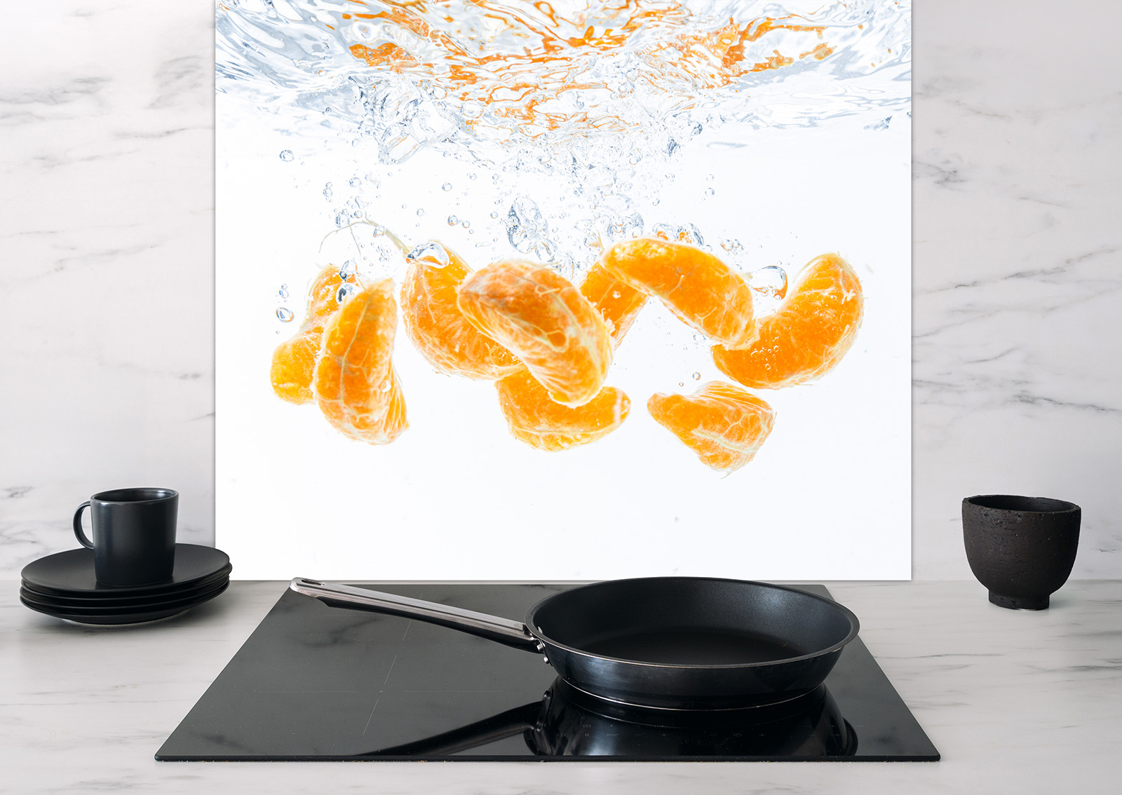 Spritzschutz Orangen von ENTDECKER mit spritzenden Orangenstücken im Wasser, im Hintergrund eine moderne Küche mit Geschirr.