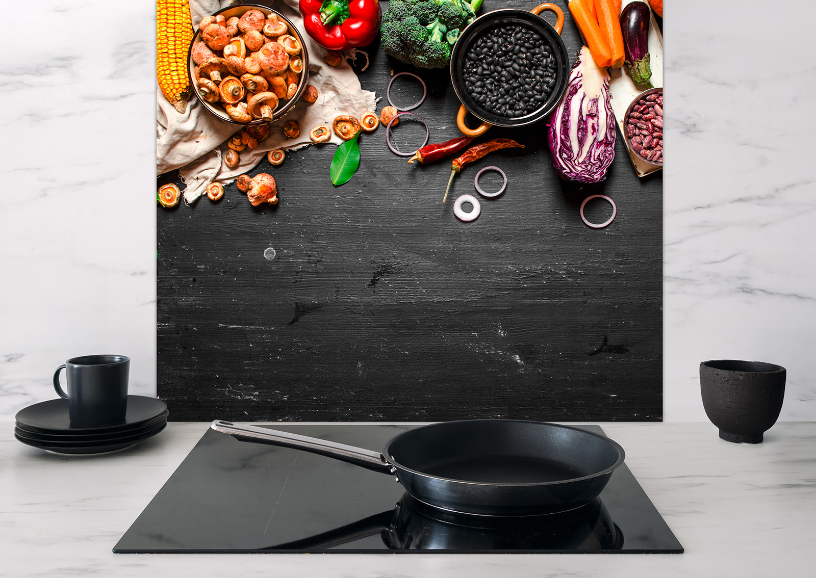 Spritzschutz Gemüsezutaten mit verschiedenen Gemüsearten und Zutaten auf einem schwarzen Tisch, Pfanne und Geschirr im Vordergrund.