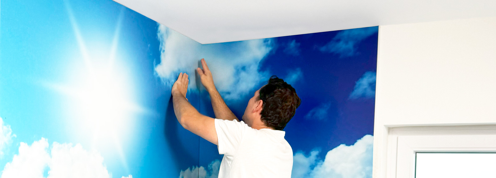 Mann bringt eine Wanddekoration mit Himmel- und Wolkenmotiv an.