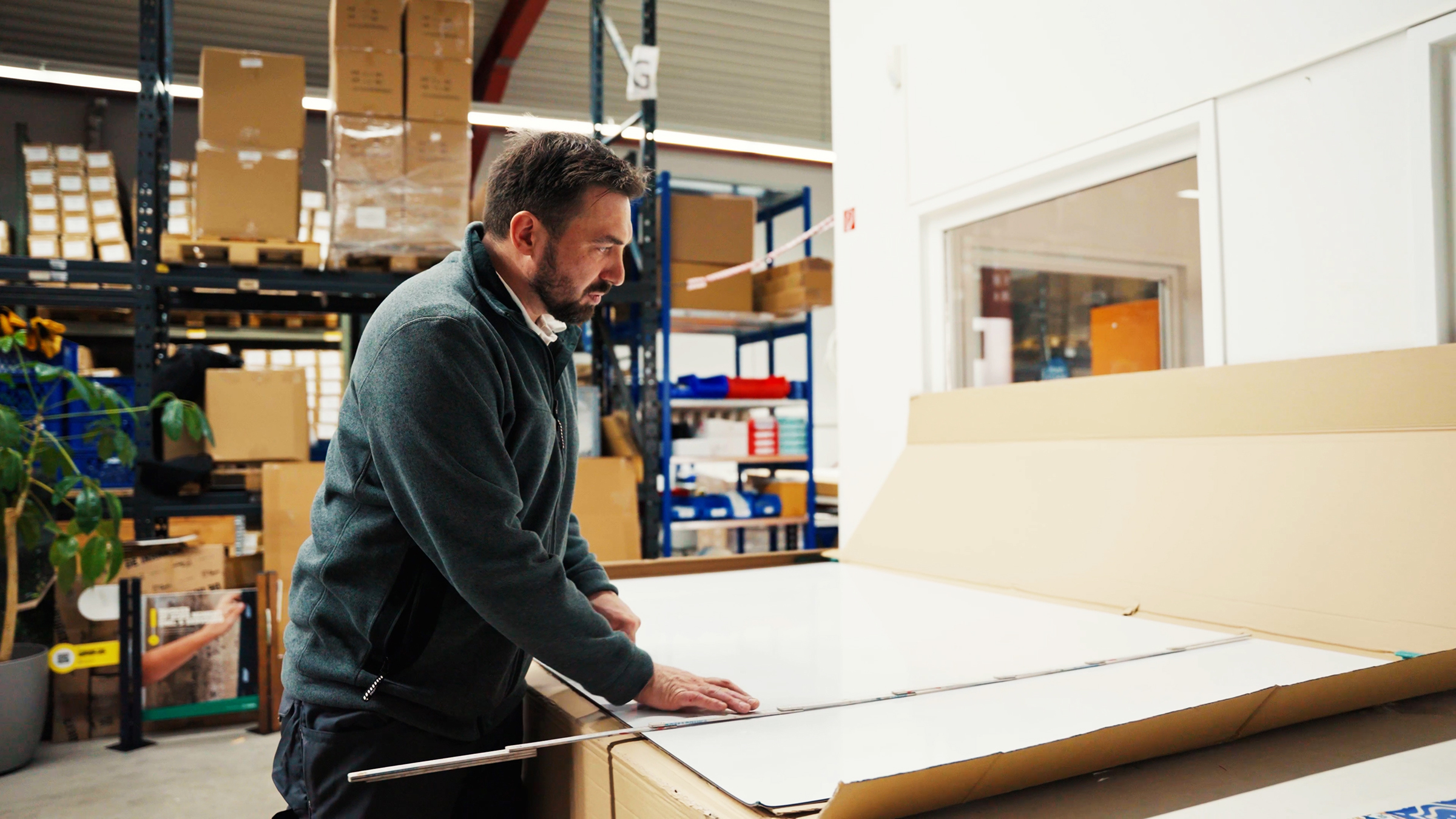 Mann in einem Lagerraum, der eine große Verpackung öffnet, um Produkte auszupacken.